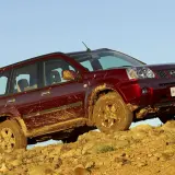 Czerwony Nissan X-Trail ubrudzony błotem podjeżdża pod skaliste wzniesienie.