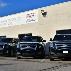 Trzy czarne Cadillac Escalade zaparkowane przed budynkiem salonu samochodowego.