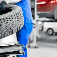 Mechanik w niebieskim kombinezonie trzyma zimową oponę na tle warsztatu samochodowego.