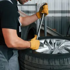 Mechanik w żółtych rękawiczkach używa klucza do demontażu opony z felgi.