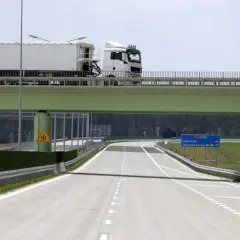 Ciężarówka na zielonym wiadukcie nad pustą autostradą z tablicami kierunkowymi.