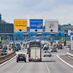 Autostrada we Włoszech z bramkami opłat, znakami Telepass i Carte, oraz samochodami w ruchu.