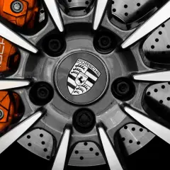 Zbliżenie na felgę Porsche z pomarańczowymi zaciskami hamulcowymi i logo marki.