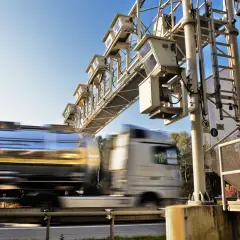 Ciężarówka z cysterną przejeżdża pod bramownicą z kamerami na autostradzie.