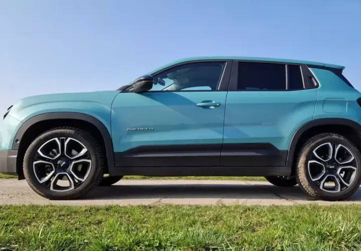 Turkusowy Jeep Avenger widziany z boku na tle nieba i zielonej trawy.