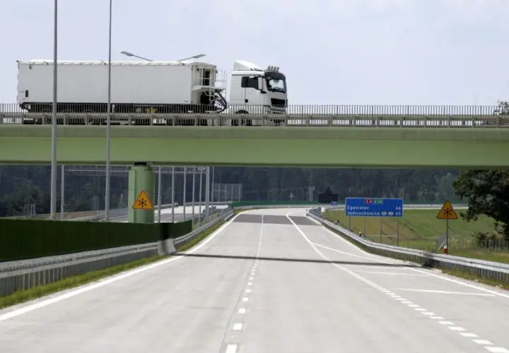 Ciężarówka na zielonym wiadukcie nad pustą autostradą z tablicami kierunkowymi.