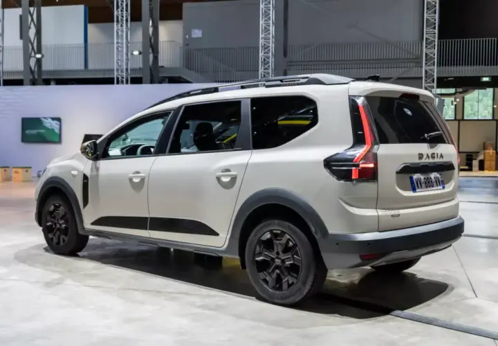 Biały samochód Dacia Jogger widziany z boku, z tyłu, na tle hali wystawowej.