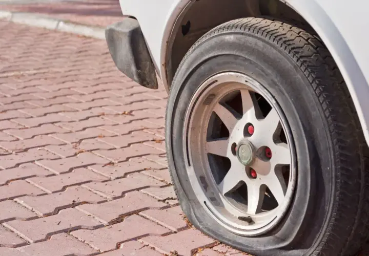 Płaska opona samochodu na felgi na czerwonej kostce brukowej.