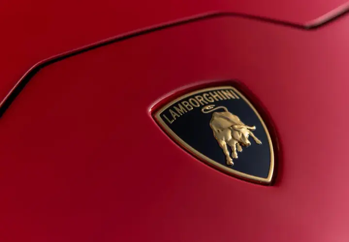 Złote logo Lamborghini z bykiem na czerwonym tle samochodu.