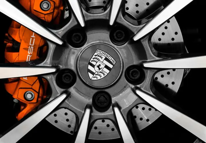 Zbliżenie na felgę Porsche z pomarańczowymi zaciskami hamulcowymi i logo marki.