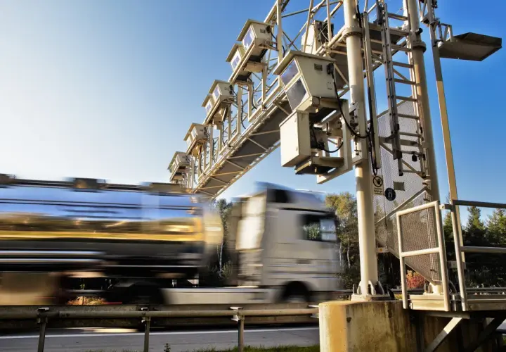 Ciężarówka z cysterną przejeżdża pod bramownicą z kamerami na autostradzie.