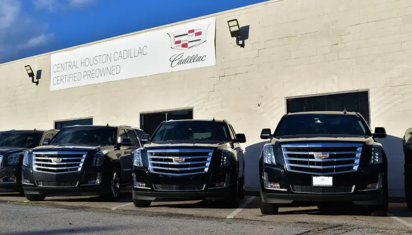 Trzy czarne Cadillac Escalade zaparkowane przed budynkiem salonu samochodowego.