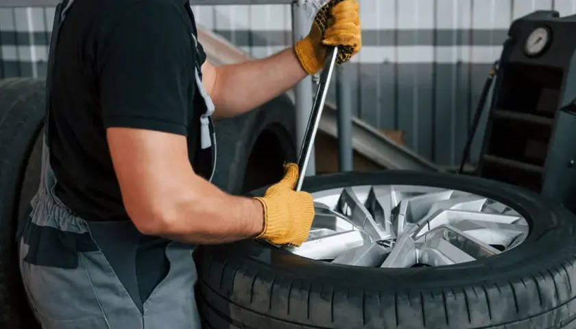 Mechanik w żółtych rękawiczkach używa klucza do demontażu opony z felgi.