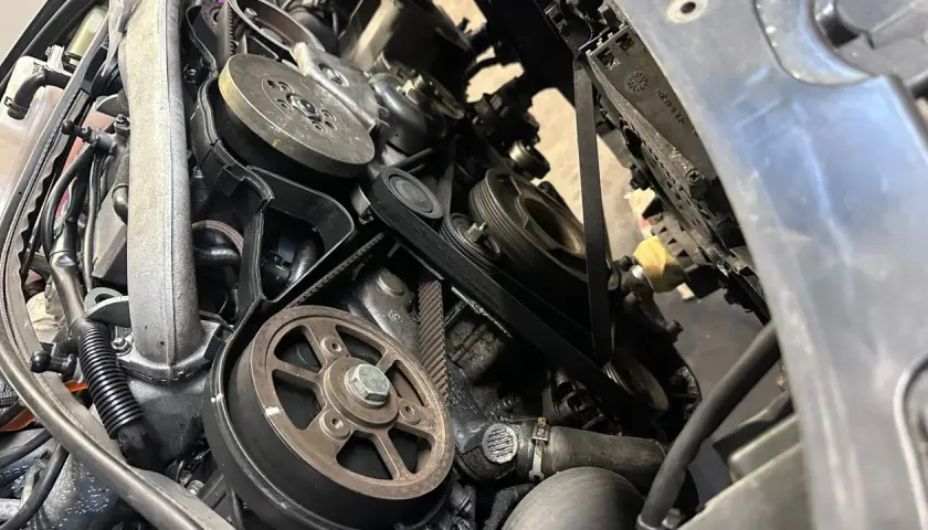 Widok z bliska na mechanizm napędu paska w samochodzie, z widocznymi kołami pasowymi i paskami.