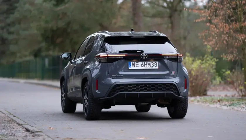 Szary Toyota Yaris Cross hybrydowy z tyłu na drodze.