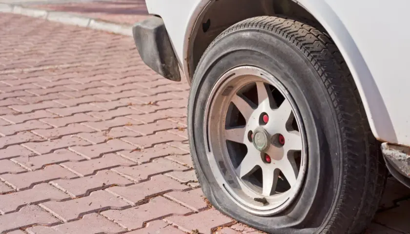 Płaska opona samochodu na felgi na czerwonej kostce brukowej.