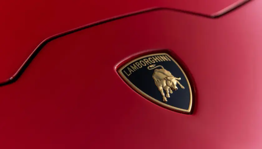 Złote logo Lamborghini z bykiem na czerwonym tle samochodu.