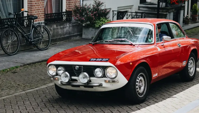 Czerwone auto sportowe Alfa Romeo z lat 70. na brukowanej ulicy, obok rower.