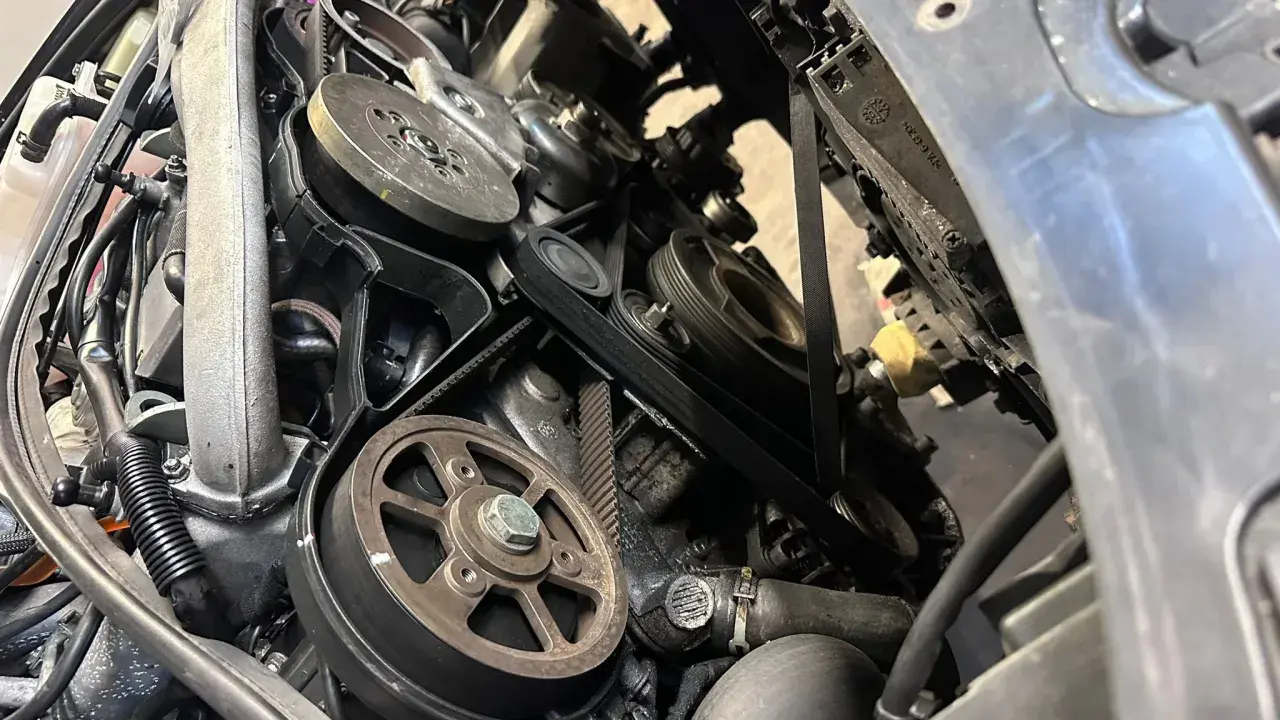 Widok z bliska na mechanizm napędu paska w samochodzie, z widocznymi kołami pasowymi i paskami.